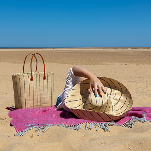 French market basket handwoven with raffia and a model wearing a raffia summer hat on a beach