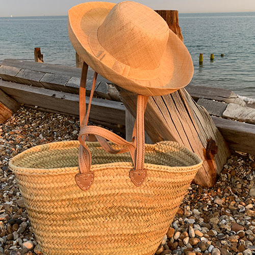 Double handle French market baskets with a raffia hat beside the sea